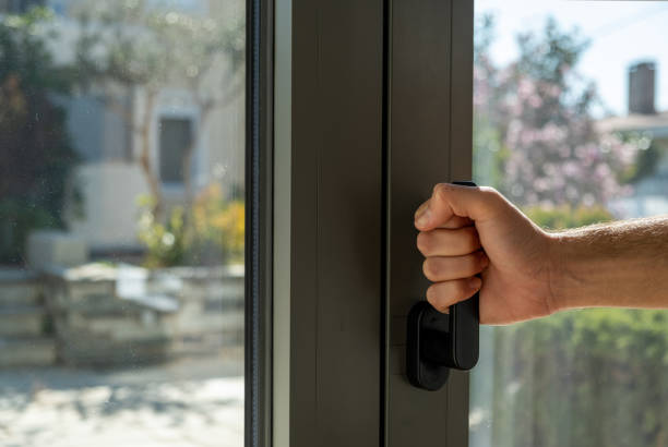 Hand holding aluminum window handle closeup view. Man opens or closes the metal or PVC door. Energy efficient, security profile, blur garden outdoor background